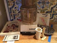 Photo showing the Cuisinart DLC-7 Super Pro food processor base with work bowl and lid, various blades, a plastic tube attachment, and the Abby Mandel's Cuisinart Classroom cookbook.