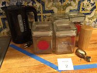 Bodum electric water boiler, six glass tea canisters, metal tea strainer, wooden tea holder on wooden counter with decorative tile backsplash