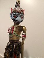 Close-up side view of the larger painted wooden shadow puppet depicting detailed facial features and cloth skirt