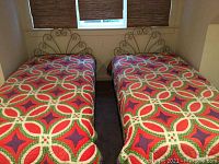 Two twin beds with gray metal scroll pattern headboards and red, white, green, and purple circular patterned quilts, showing full beds and placement.