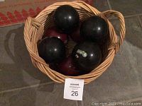 Top-down view of four black and four maroon bocce balls inside a woven basket on stone floor.