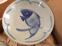 Blue fish pattern on a pottery dinner plate with abstract swirls on cream surface.