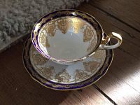 Close-up of teacup and saucer showing cobalt blue border and intricate gold filigree inside cup and around saucer edges. Gold gilt handle detail.