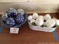 Blue and white decorative bowl with six blue and white patterned spheres next to white ceramic basket with ceramic fruit pieces