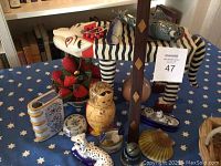 Photo shows wooden decorative cat, Russian nested doll, glass candy dish, ceramic dog figurine, and other decorative items on a blue star-patterned tablecloth.