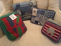 Four decorative needlepoint pillows shown on a beige textured chair, displaying different designs and colors.