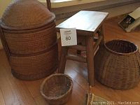 Wide view of large round woven basket with lid, medium basket, smaller baskets, and wooden stool on wooden floor