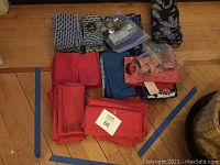 Photo showing folded red and blue cloth napkins with assorted napkin rings in plastic bags and some patterned napkins.