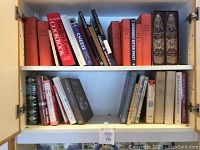 Image showing two shelves filled with assorted cookbooks of various colors and bindings, mostly hardcover, some vintage editions.