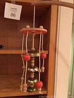 Close-up of one wind chime showing wooden beads, red spherical accents, and metal gold-painted bells hanging from beige cords attached to a round wooden top colored beige and red.