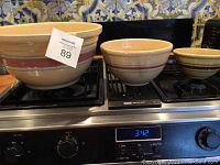 Three ceramic mixing bowls set on a stove, including large bowl, medium bowl with visible damage, and smaller different design bowl