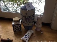 Full view of the lot showing large blue and white flower vase, cork-top jar, decorative potpourri jar, and wall plant holder on wooden floor near window.