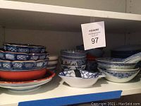 Shelf view showing multiple stacked serving bowls in blue and white designs with some reddish bowls underneath.