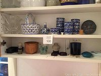 Wide shot of shelf with ceramic sauce containers, ceramic basket, woven basket, glass dishes and other small decorative pieces.