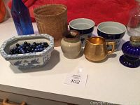 Lot showing porcelain planter filled with black and blue marbles, woven container behind, various small decorative vessels, blue glass bottle and clear bottle to the sides