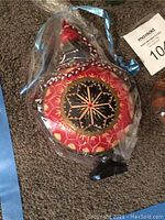 Painted wooden flask showing geometric and animal designs with blue decorative tie on carpeted floor