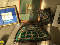 Photo showing several framed artworks on a couch including a 3D fabric artwork depicting a garden scene below other framed art pieces