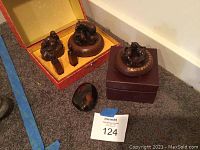 Wide shot of carved wooden Buddha, rams on base, two small figurines on stands, small polished stone, all arranged on display box interior.