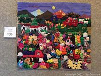 Photo of handmade colorful 3D cloth tapestry depicting a busy market scene with numerous fabric produce and small figures under a mountain landscape.