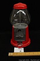 Front view of red gumball machine with clear globe and metal front mechanism with handle.