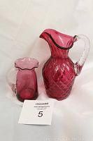 Photo of the two cranberry glass pitchers side by side, showing size difference and overall design.