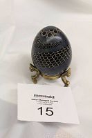 Front view of dark Fabergé style decorative egg on brass stand, showing honeycomb and wave-like white patterns.