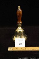 Front view of brass bell with wooden handle, showing polished surface and shape.