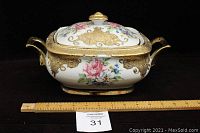 Porcelain serving vessel with floral and gold designs from front with measuring ruler for scale