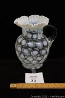 Front view of Fenton white opalescent pitcher with coin dot pattern and ruffled trim, showing overall shape and handle.