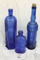 Front view of the three cobalt blue glass bottles including the embossed Milk of Magnesia bottle, the mid-sized textured bottle, and the tall ribbed bottle with cork.