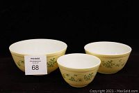 Set of 3 vintage Pyrex mixing bowls of descending size, light yellow exterior with green vine and daisies, white interior.