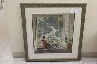 Full view of the framed print showing the woman sitting on a porch with large window view and textured silver frame.