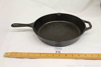 Cast iron skillet angled showing full cooking surface and handle next to ruler for scale