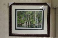 Full view of the framed print 'The Blue Heron' showing the artwork with green forest and heron reflected in water within an ornate dark wood frame.