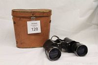 Black Army and Naval Special binoculars positioned beside a well-worn brown leather carrying case with top flap closed