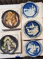 Five Bradford Exchange Christmas-themed collector plates with various holiday scenes laid out in their boxes. Visible warping on some plates.