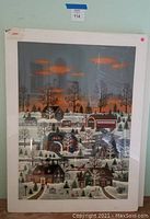 Full view of one serigraph print showing a winter village scene with houses and covered bridge under a sunset sky.