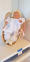 Photo of Borjusa life-like rubber baby doll lying in rattan doll carrier showing detailed facial features and white clothing with bonnet