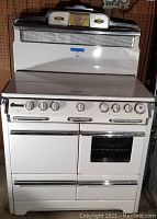 Front view of the vintage white enamel and chrome gas stove showing control knobs and oven doors.