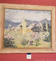 Front view of framed oil painting showing desert landscape of cacti, shrubs, boulders and mountains.