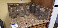 View of ten clear glass Kerr quart canning jars with metal lids arranged on a kitchen counter.