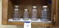 Four vintage Atlas canning jars arranged in a row on a shelf, three larger quart jars and one smaller pint jar.