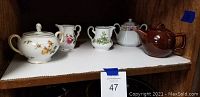 Shelf with the complete lot showing Rosenthal Charlene sugar bowl with floral decoration, two floral creamers, brown McCoy pot, and ceramic teapot.