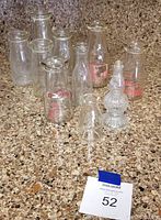 Eleven vintage milk and glass bottles arranged on countertop, some with printed slogans and brand markings