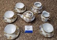 Overview of entire Nippon tea set on brown textured surface showing teapot, creamer, sugar bowl, five saucers, four cups with one repaired cup