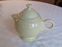 Large ivory-colored Fiesta teapot on table, side view of spout and handle