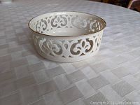 White Lenox porcelain reticulated bowl with intricate openwork pattern and gold rim, shown on a white textured surface.