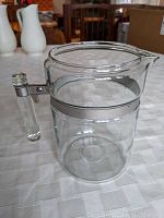 Front and side view of clear Pyrex glass coffee pot with straight rod glass handle and metal band around top. Missing lid and percolator insert.