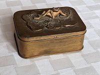 View of the antique rectangular hinged tin box with frog figure on lid from an angle, showing shape and hinged lid.