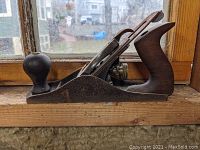 Side view of the antique Bailey No. 3 wood plane showing metal body, wooden front knob and rear handle, and blade assembly.